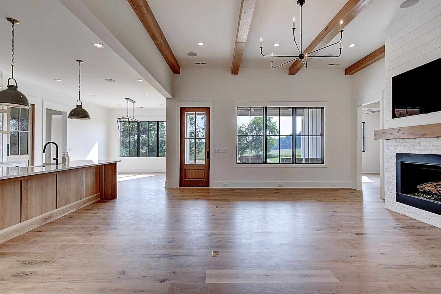 Spacious, modern living room with wooden beams, large windows, and a cozy fireplace. Light hardwood floors.