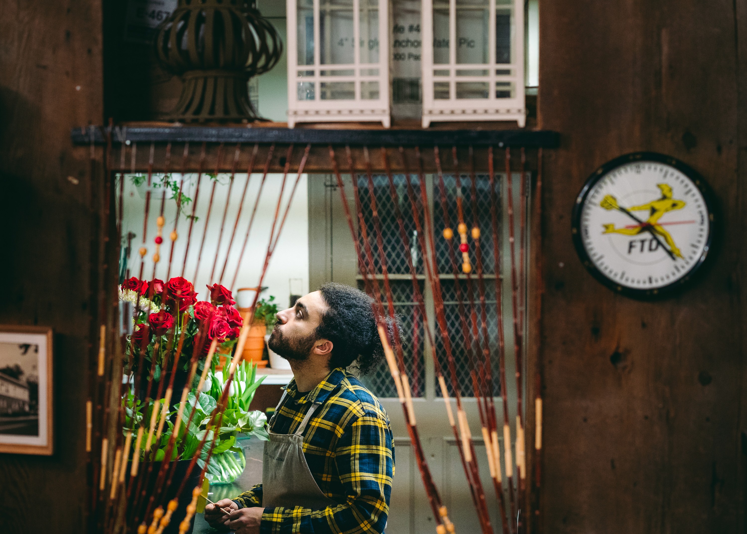 Un jeune homme dans son uniforme de fleuriste contemple la boutique. Joué par Anas Hassouna. Scène tirée de la série Web Les Fleuristes