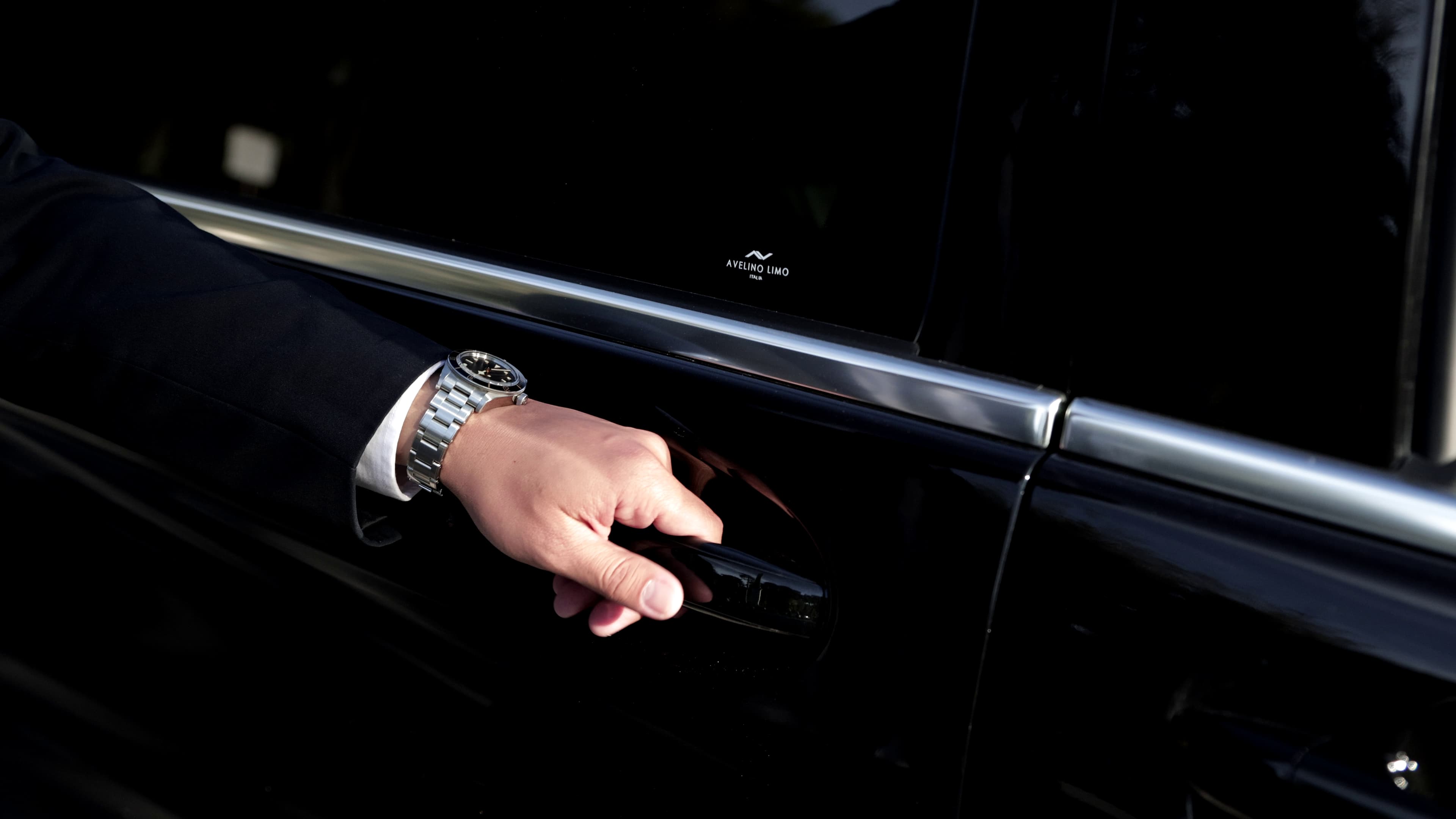 Chauffeur holding on to the handle of a vehicle with an icon of Avelino Limo Italia in the window.