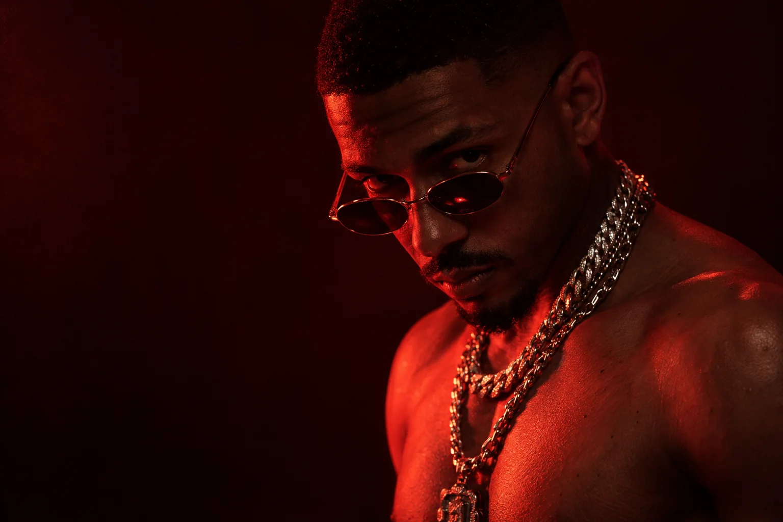 Man in tinted sunglasses and silver chains in deep red light