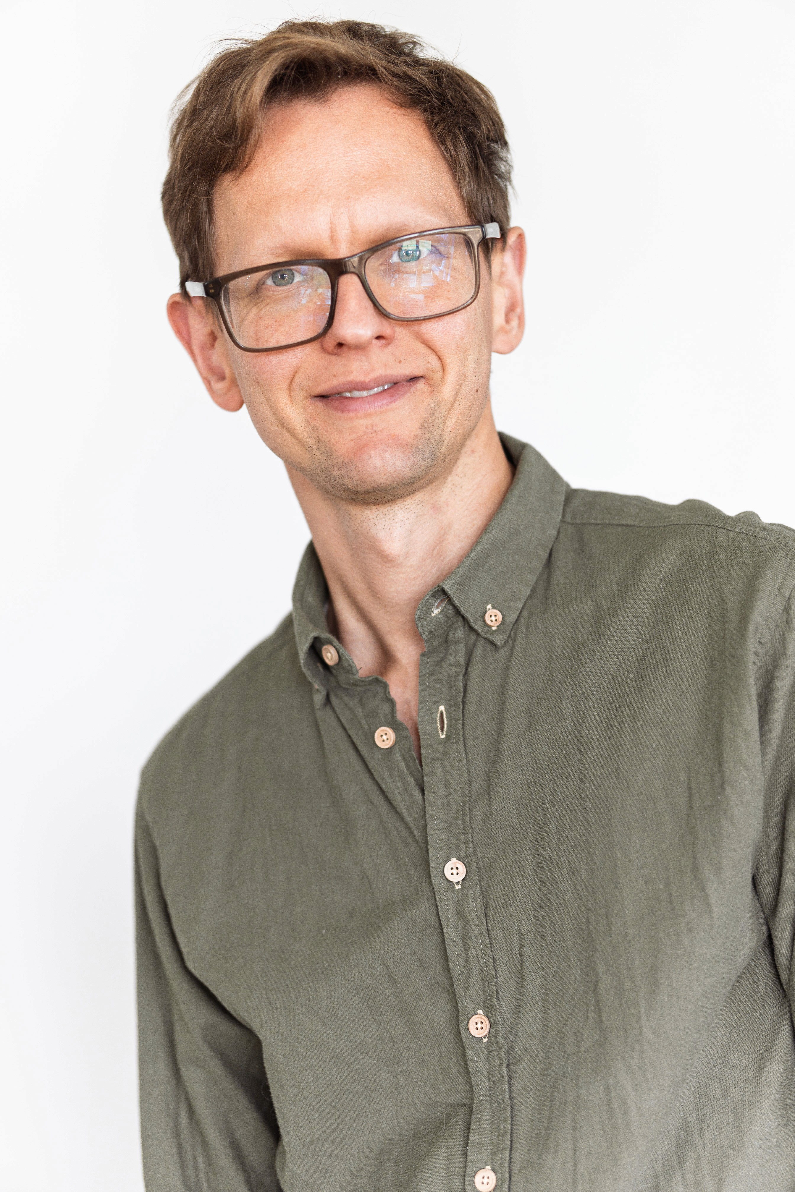 Zdjęcie przedstawia kobietę o jasnych, falowanych włosach i okularach w ciemnych oprawkach. Ma na sobie czarną bluzkę z wzorem i patrzy prosto w obiektyw. Tło jest jednolite, ciemne.