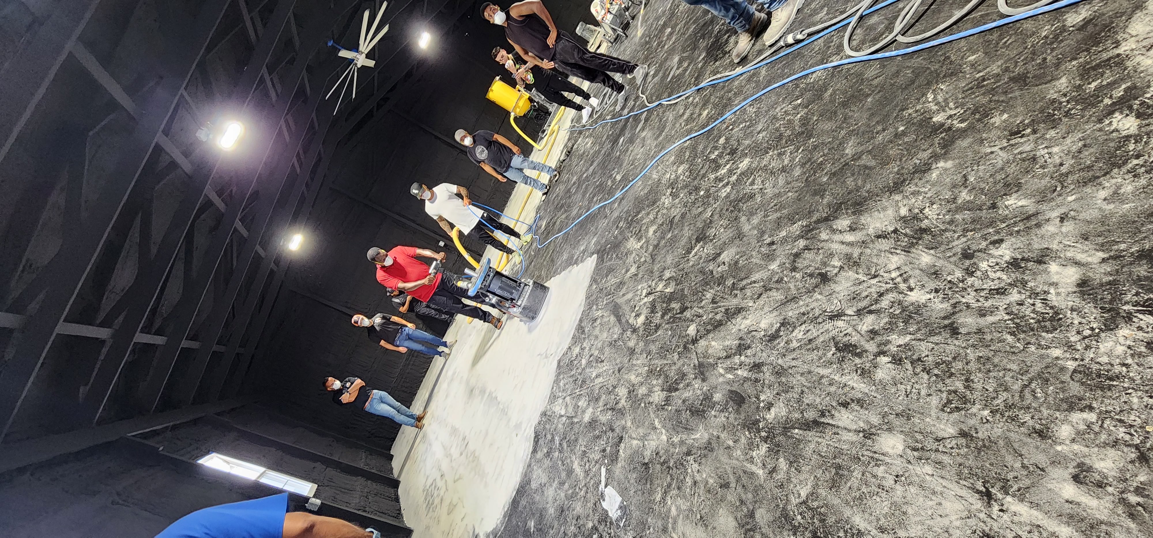 A participant operates a concrete floor grinder while the workshop group watches.