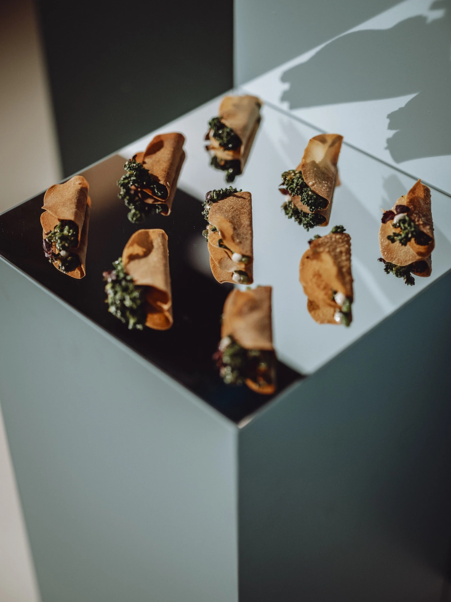 Filled pastry rolls arranged on a mirrored cube pedestal.