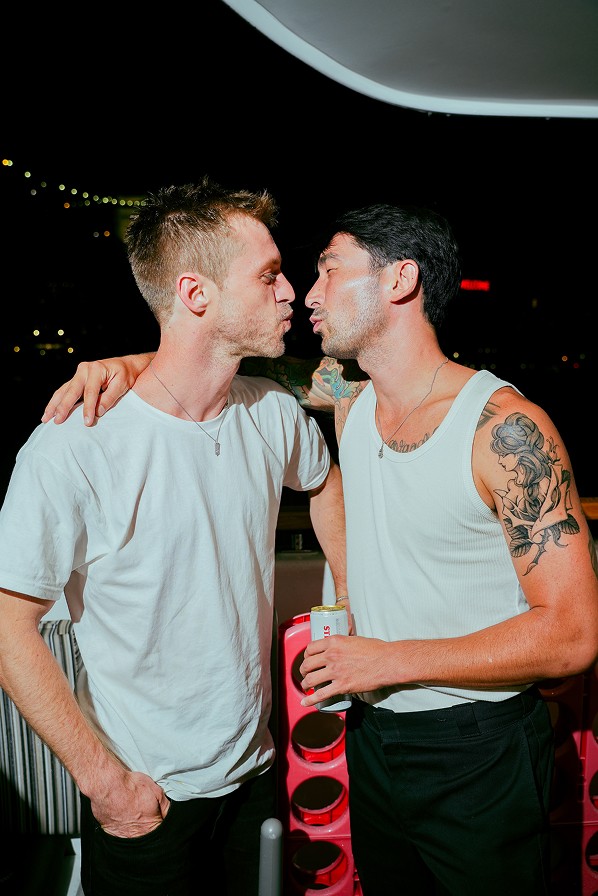 Two young men lean in close, sharing a playful moment, with one wearing a sleeveless shirt and the other in a t-shirt.
