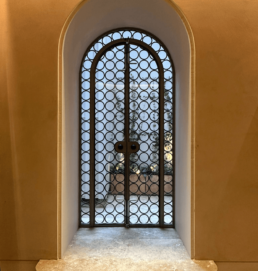 A decorative arched window with intricate metalwork, set in a warm-toned wall, showcasing light filtering through.
