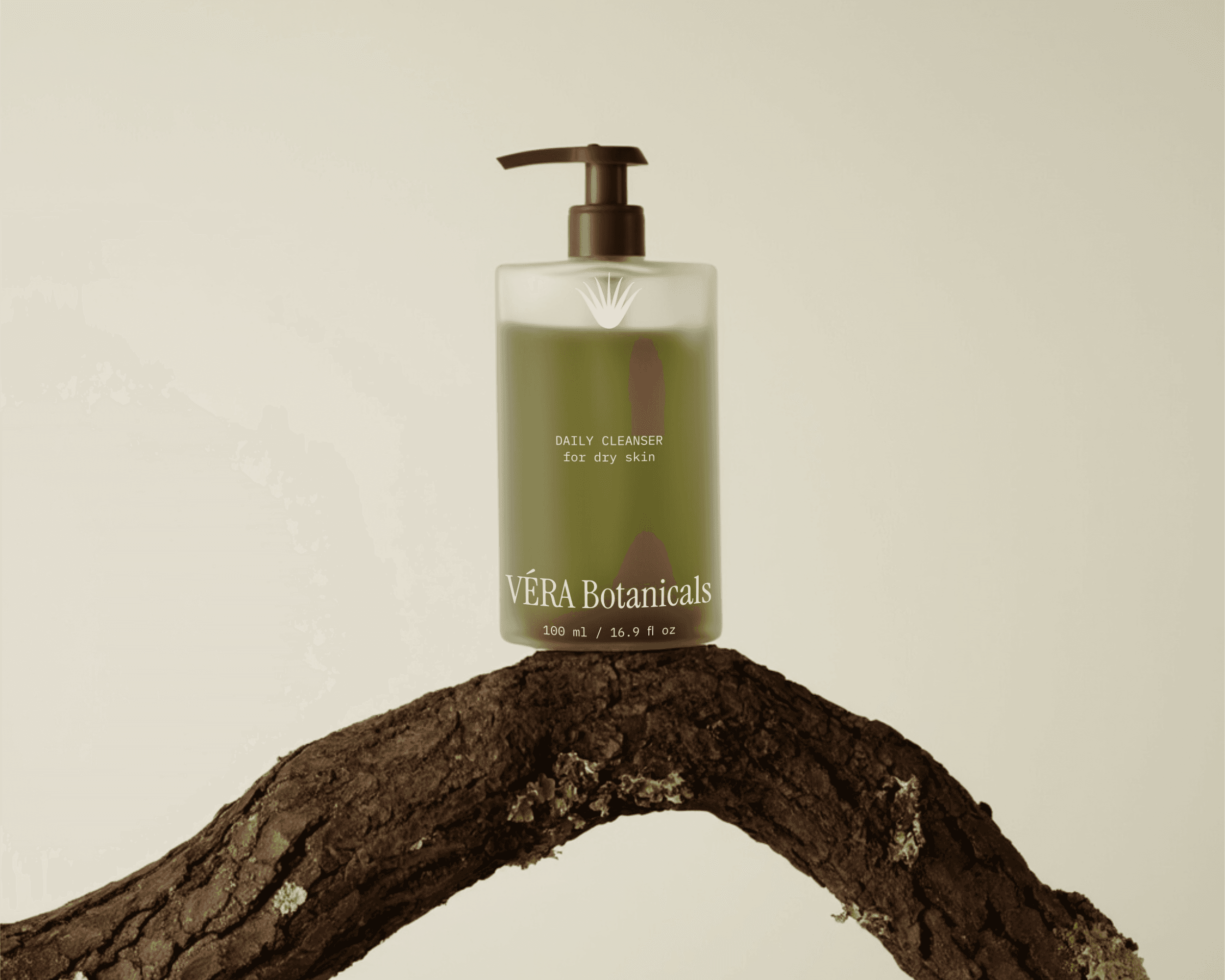 A packaging bottle design for the organic skincare brand VÉRA Botanicals. The bottle features a frosted glass finish and is filled with olive-green liquid. The bottle is sitting on a branch.