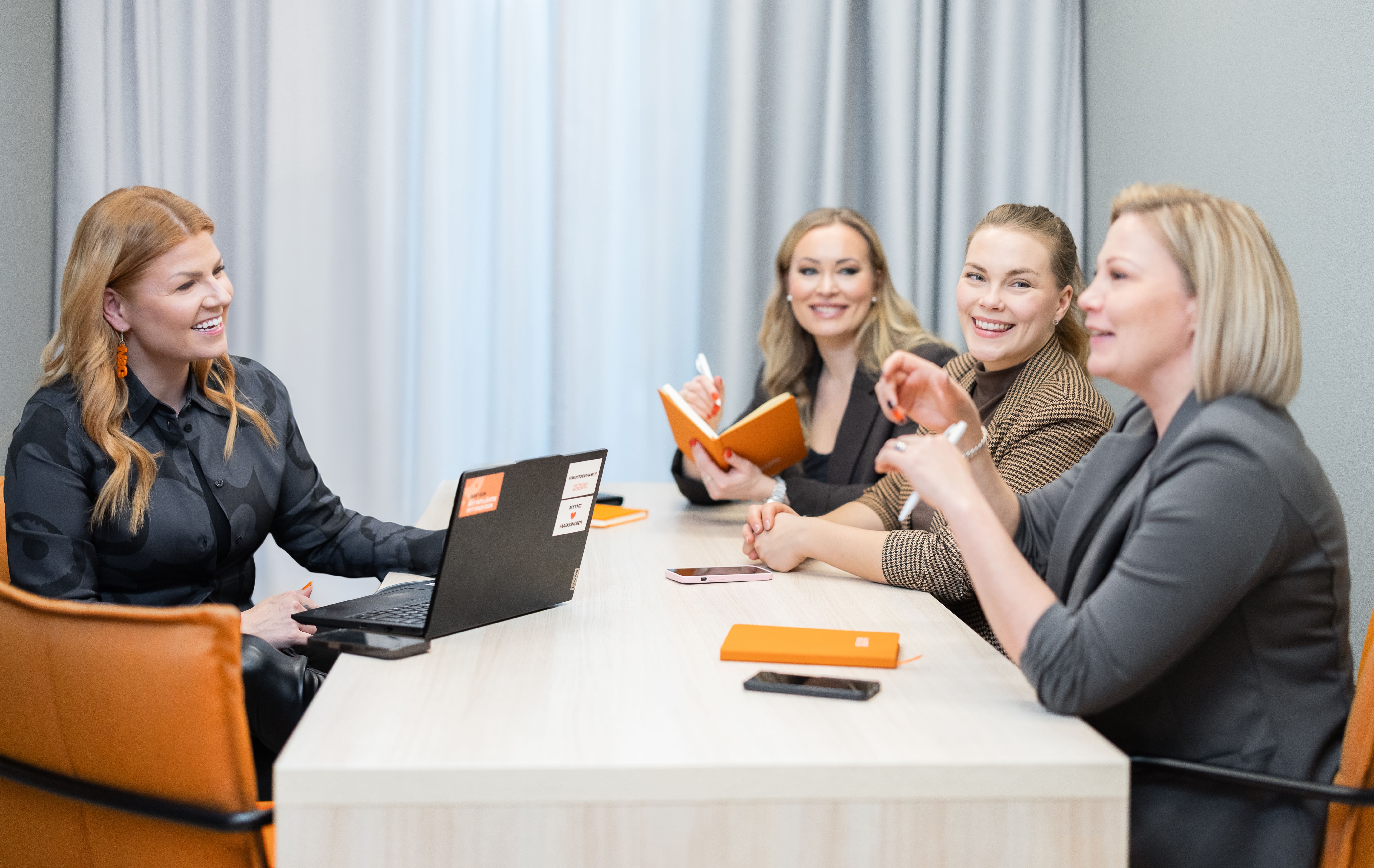 Neljä Network & Growthin valmentajaa keskustelee pöydän ääressä; läppäri, muistiot ja kahvit – taustalla vaalea verho.