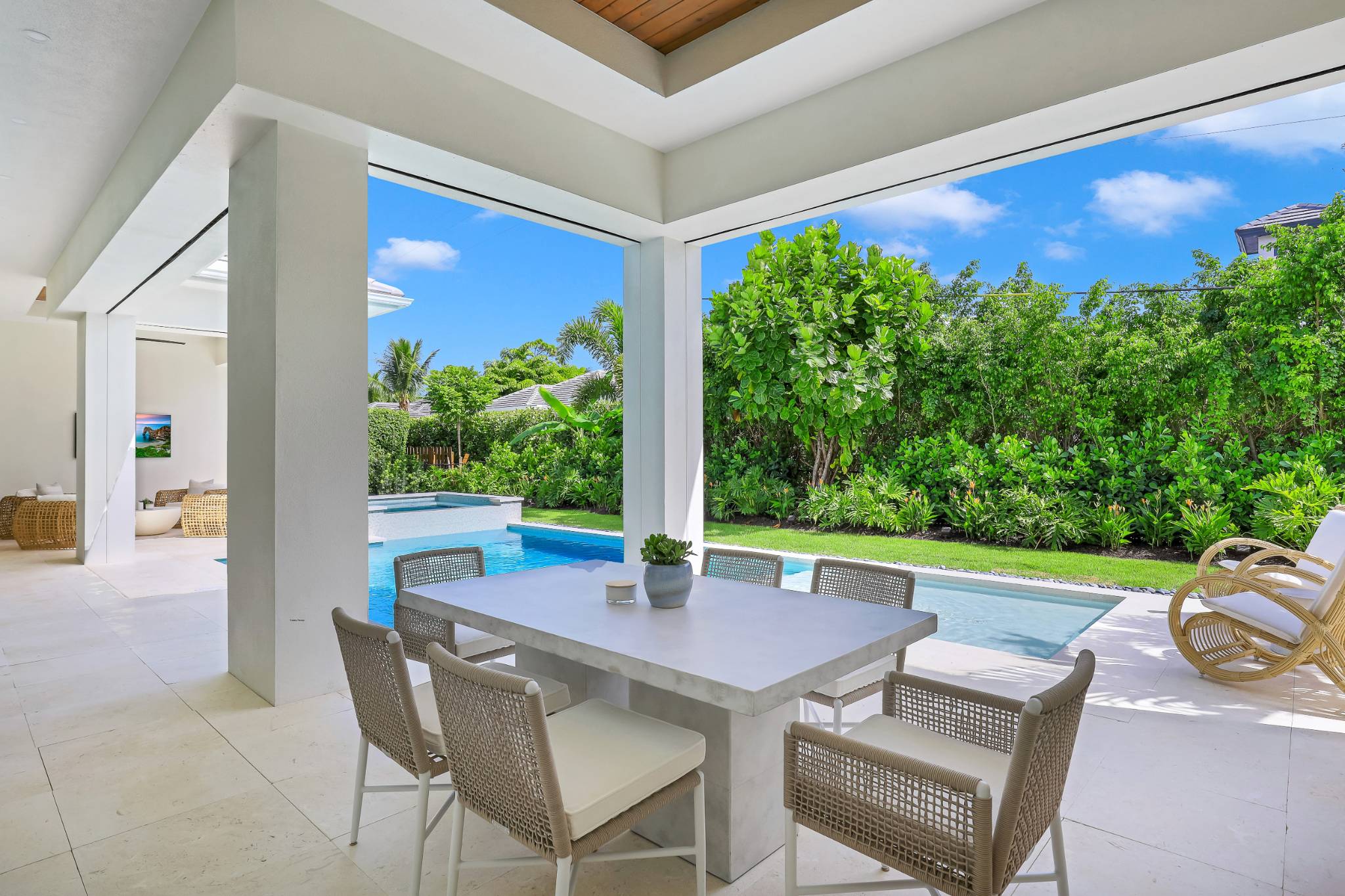 a outdoor lounge area next to a pool with trees lining the property in the background