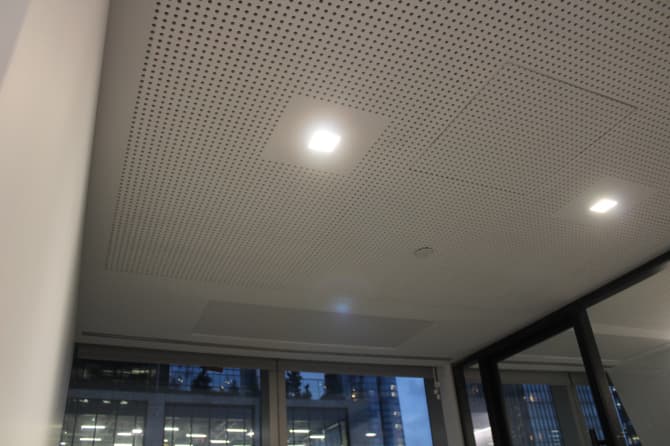 A ceiling with a design made of small holes and a single built in light fixture