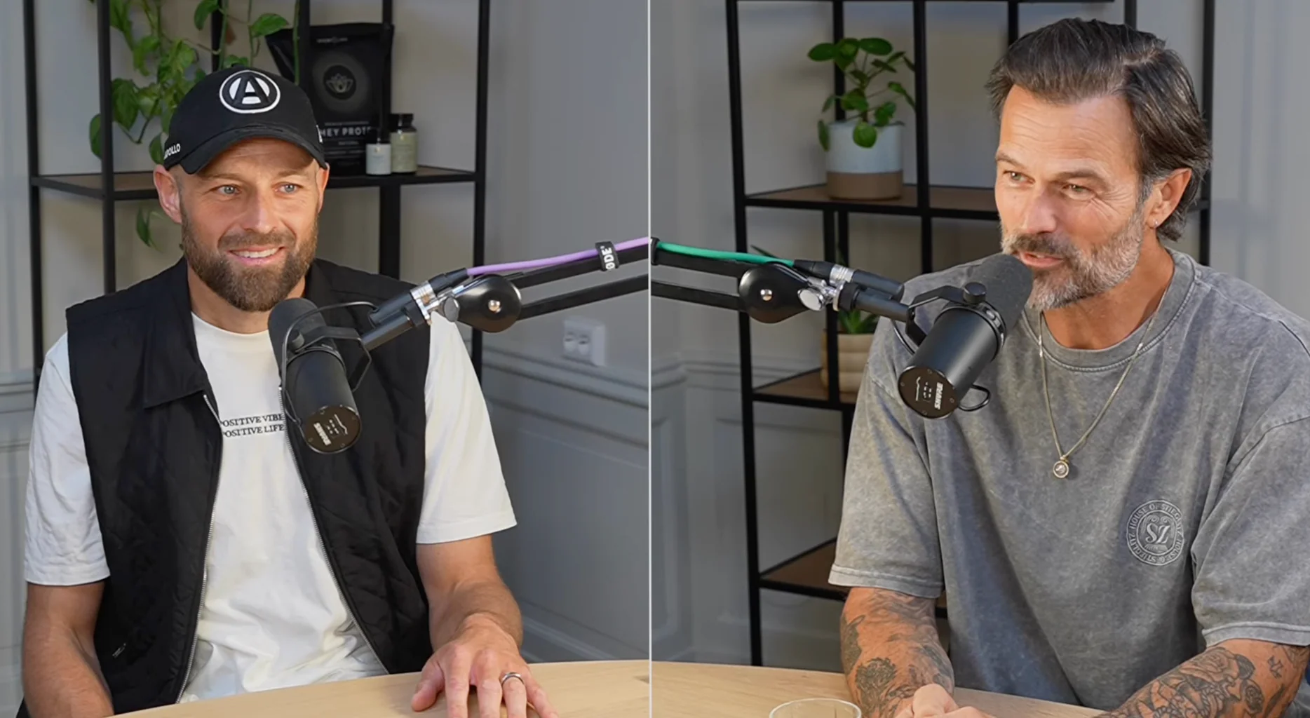 Ramon Siljade en Arie Boomsma in gesprek tijdens een podcast-opname, elk achter een microfoon aan een tafel in een lichte studio-omgeving.