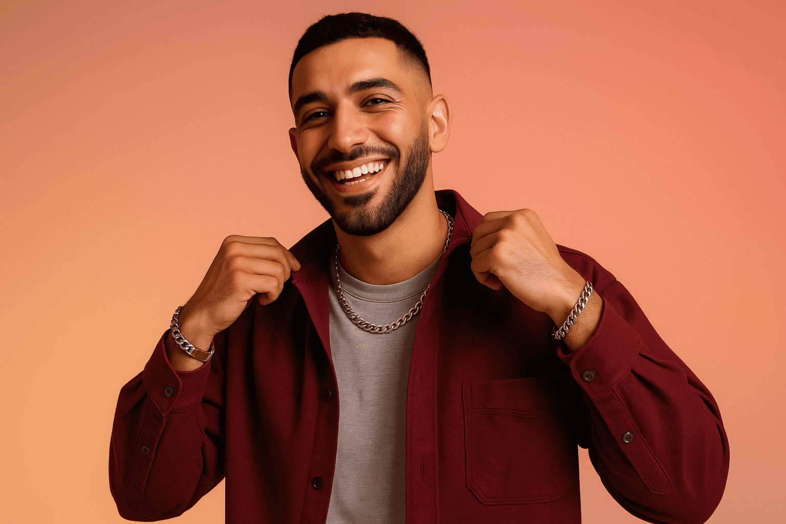 Smiling man in a burgundy jacket and t-shirt, adjusting his collar while standing against a soft orange gradient background.