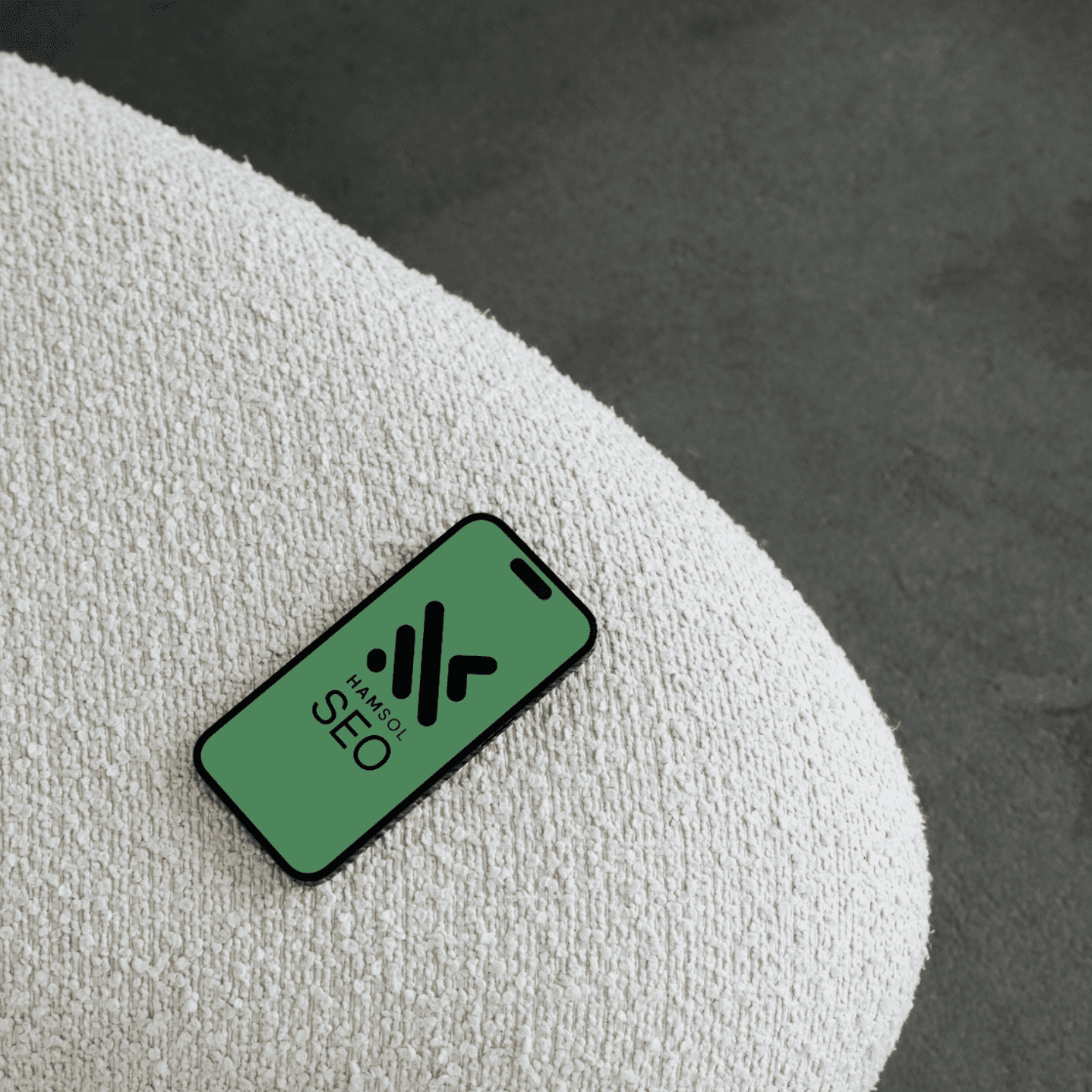 Iphone resting on soft white surface dispalying a green background with the Hamilton Solutions logo and the title SEO.