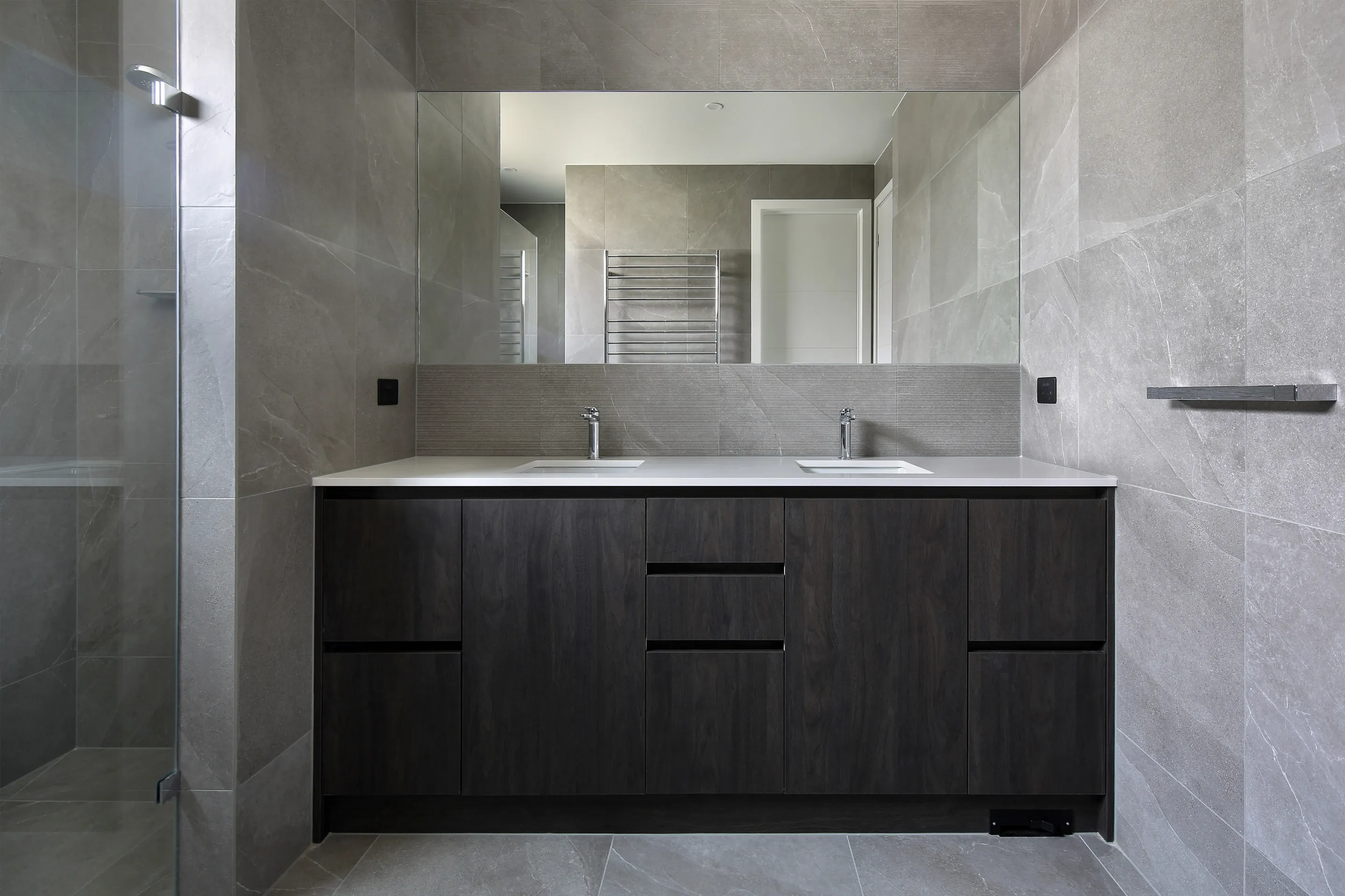 Bathroom with grey stone-look tiles, a charcoal-grain timber double vanity with white stone top, large mirror and a glass shower