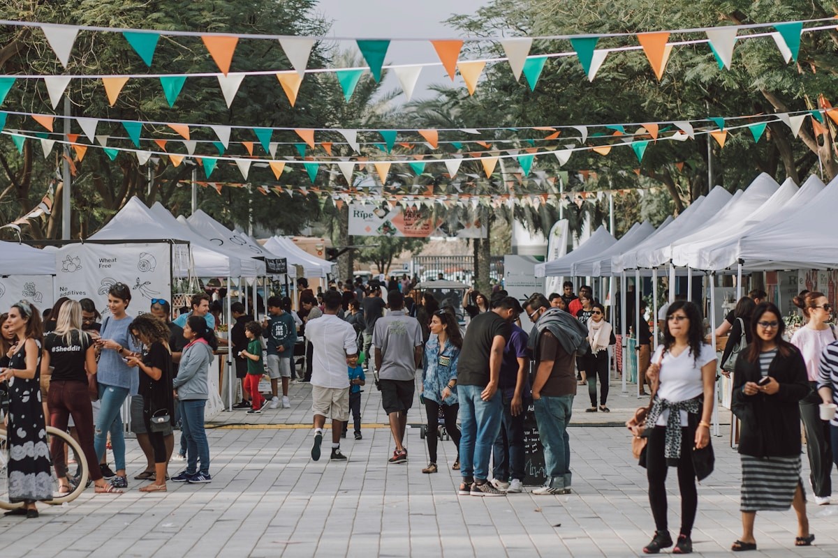 A wide view of a diverse community street festival with vendor tents and colorful bunting