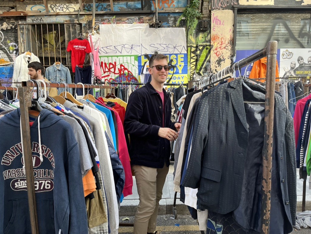 An image of me in between racks of clothing at a thrift store.