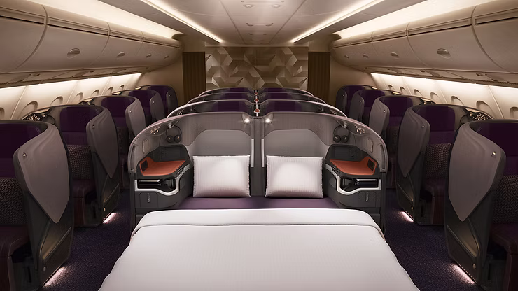 Singapore Airlines long-haul Business Class cabin showing the bulkhead seats configured into a double bed with plush purple upholstery and warm mood lighting.