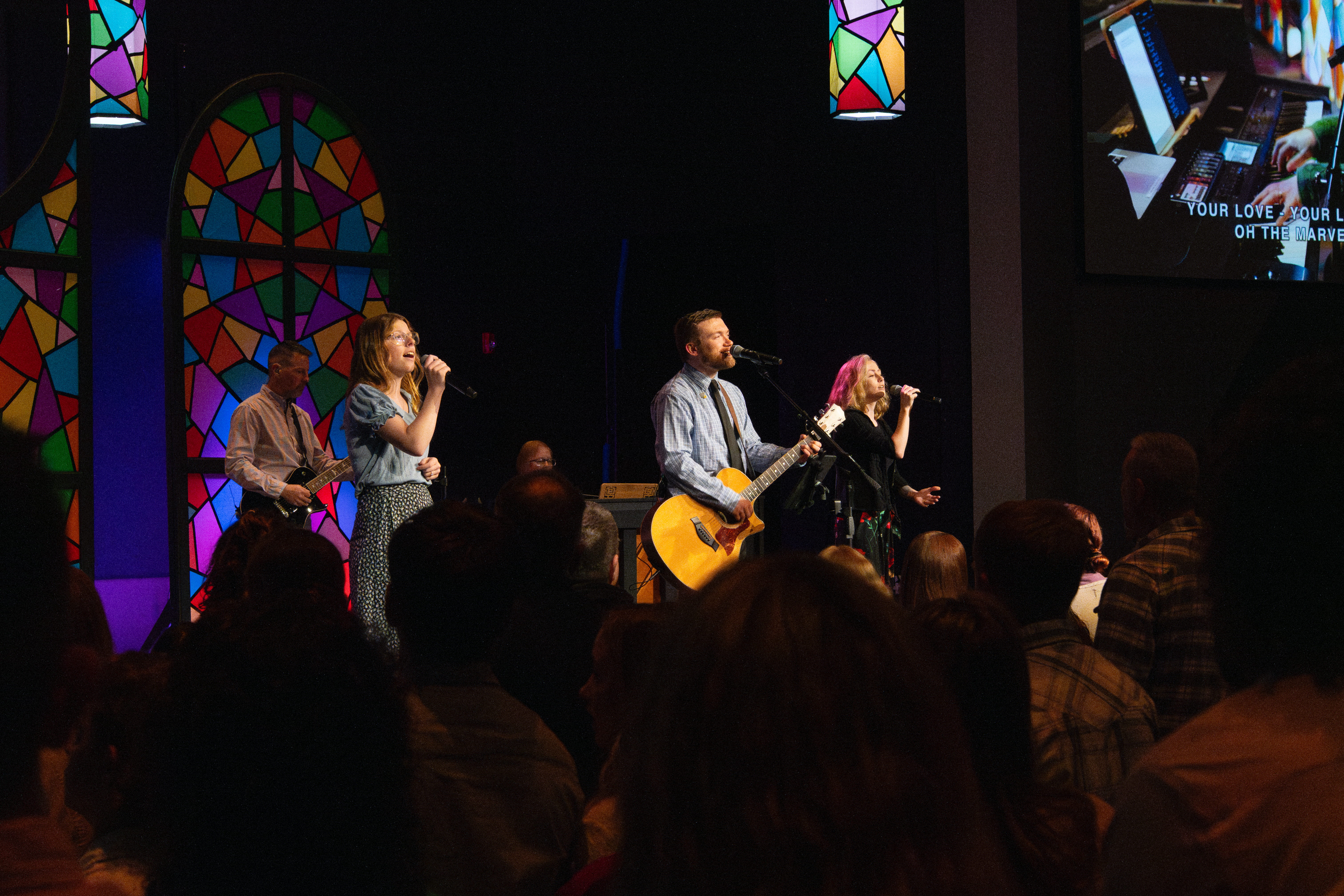 Photo of worship service with singers and musicians playing instruments on stage.