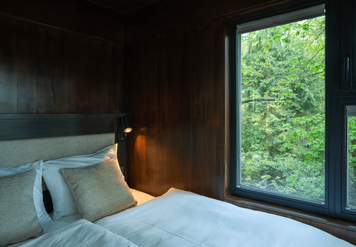 Cozy bedroom with a wooden interior and large window overlooking lush greenery outside.