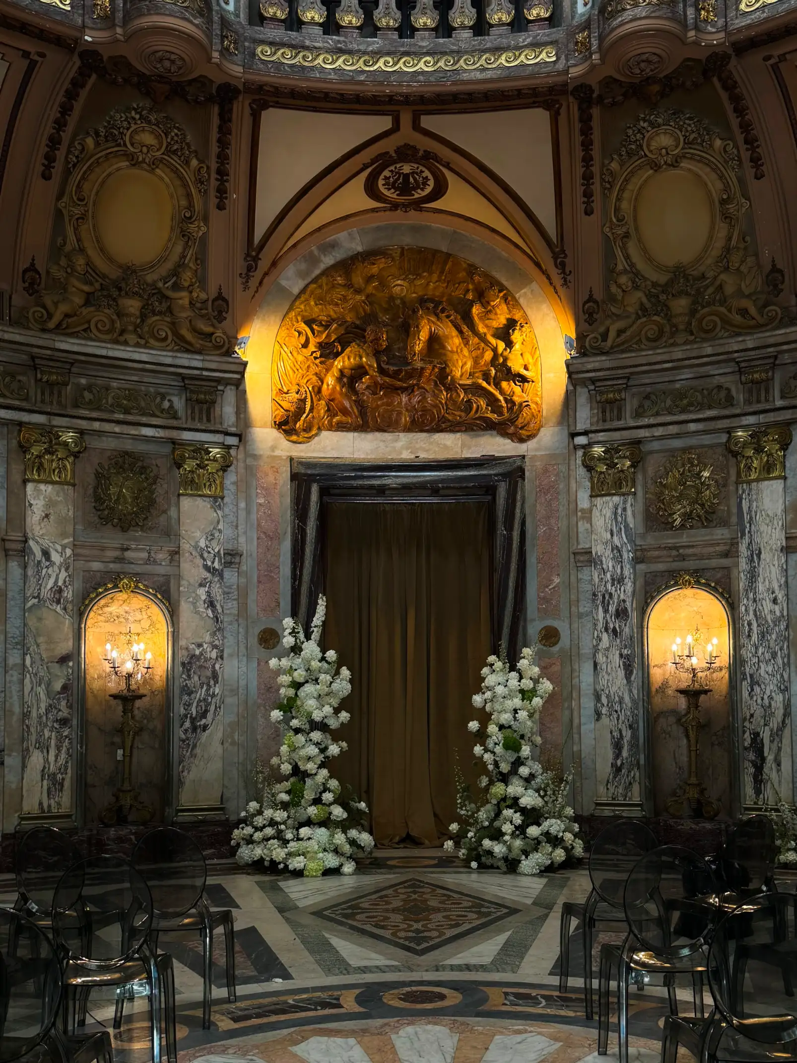 Instalación floral blanca en salón histórico con arquitectura ornamental para evento institucional, creando atmósfera majestuosa.