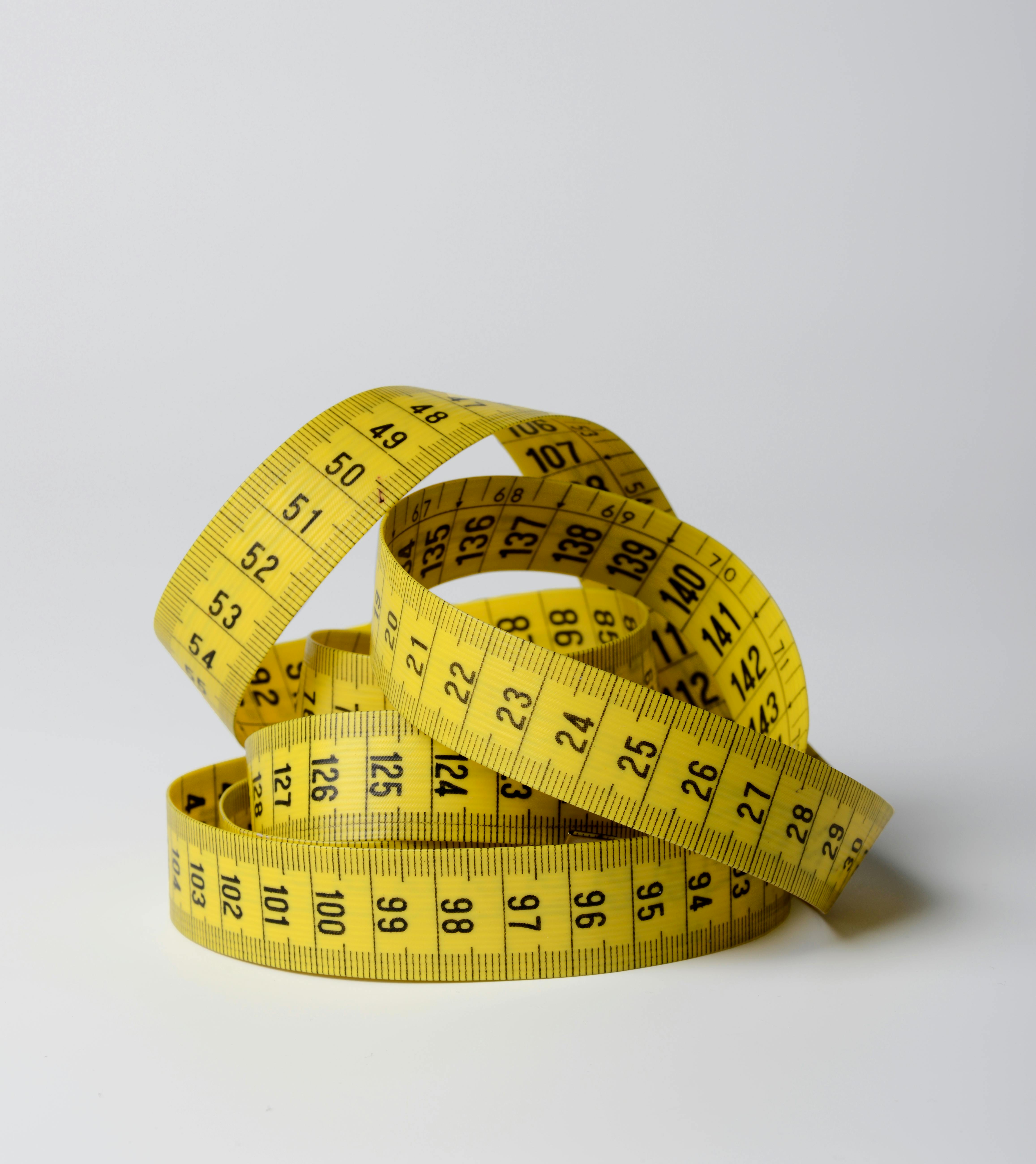 Yellow measuring tape coiled on a white background, symbolizing measurement and evaluation.