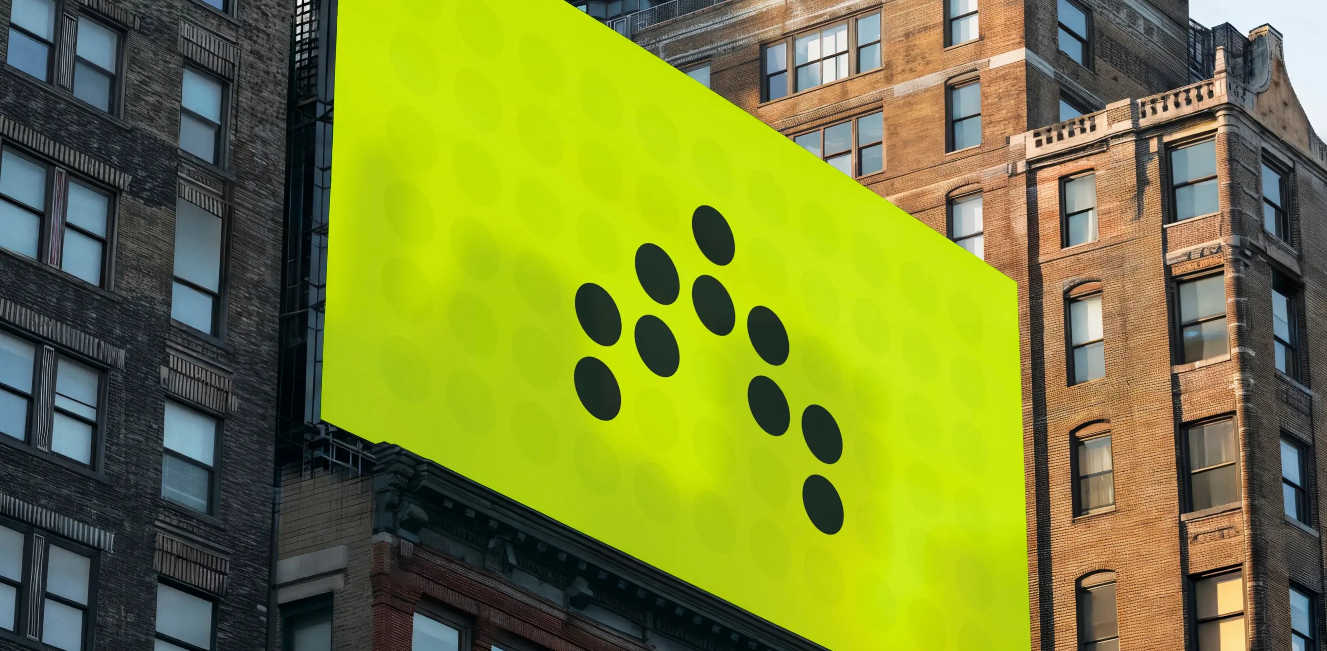 A large, bright green billboard with a minimalist design featuring black dots arranged in a pattern, displayed on the side of a tall urban building. The billboard stands out against the surrounding brick and concrete structures, with windows and architectural details visible.