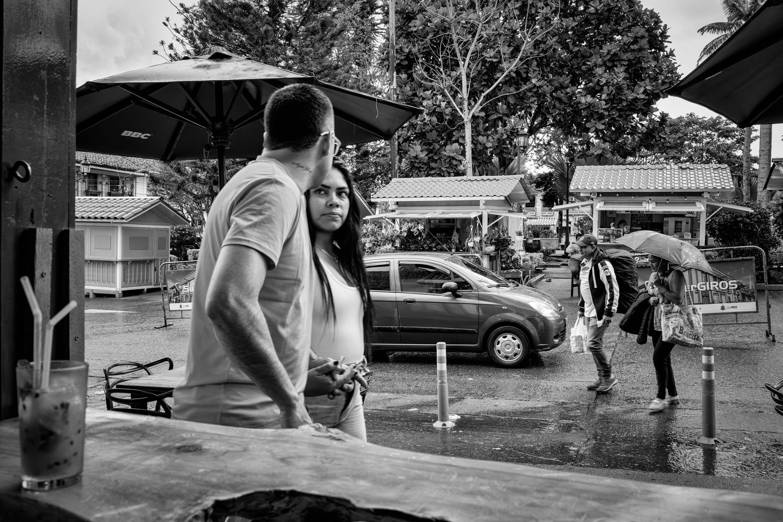 Rainy street scene with people passing by a bar window.
