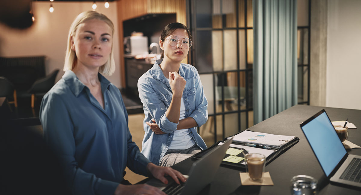 Two women listening attentively during a team meeting with laptops and documents on the table