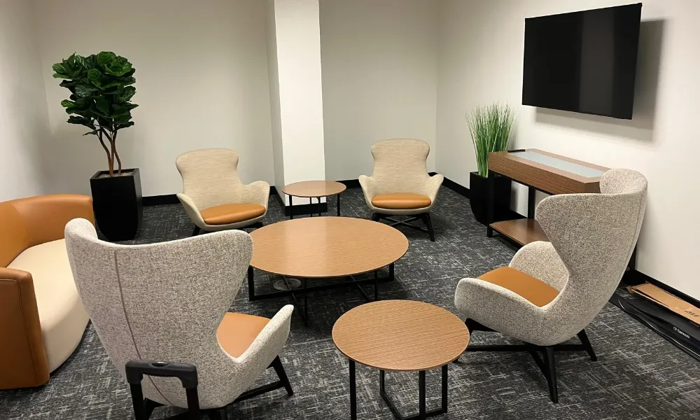 Modern lounge area with gray wingback chairs, round wooden tables, and a wall-mounted TV.