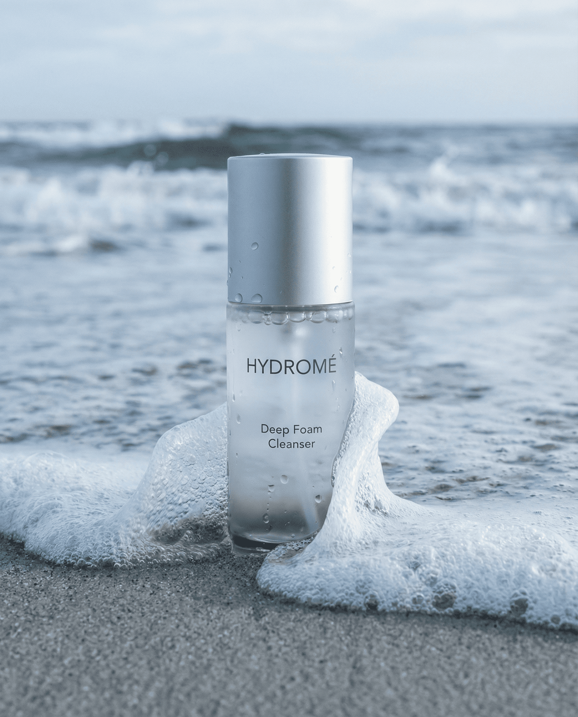 Hydromé Deep Foam Cleanser bottle on beach with sea foam and ocean waves