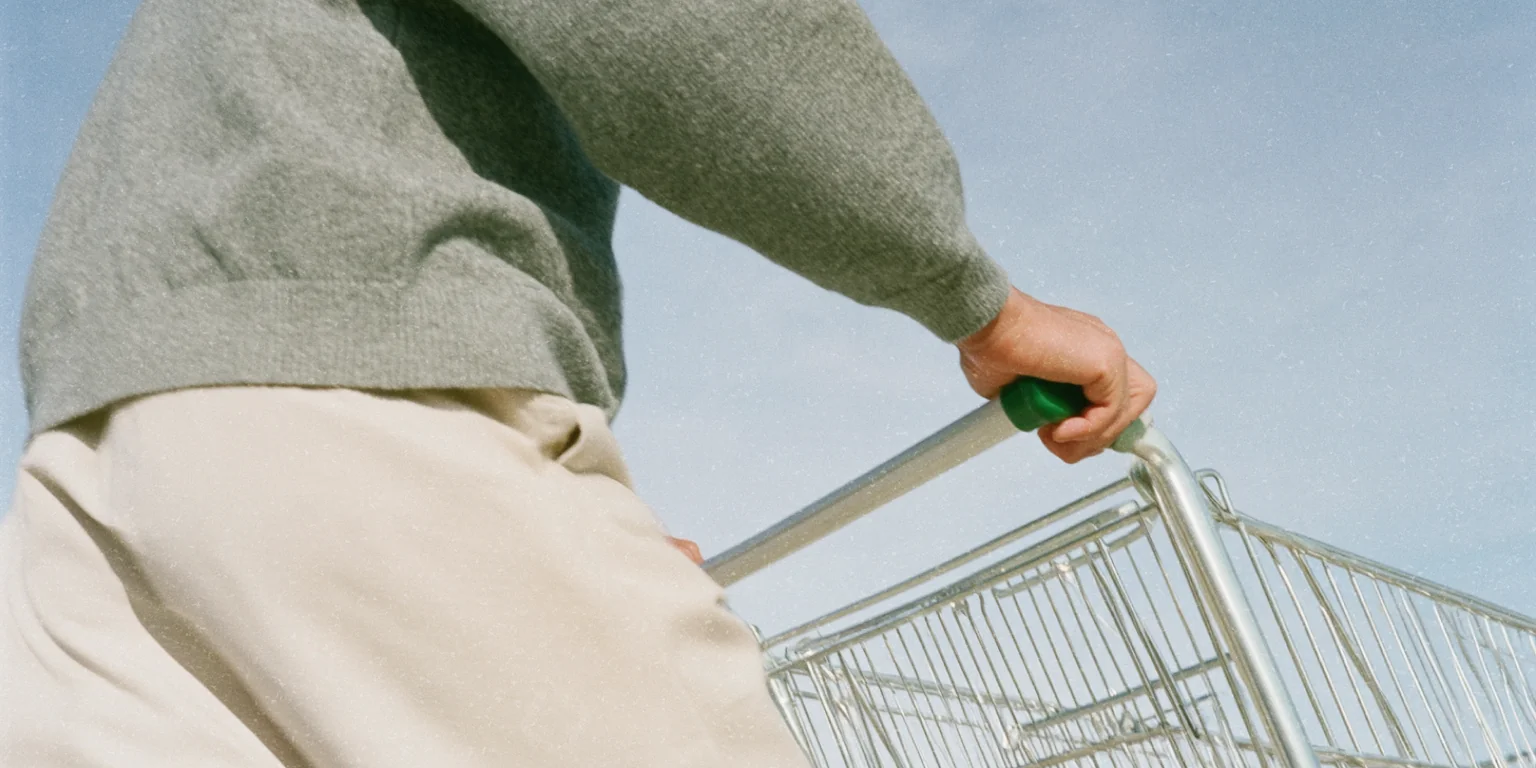 Person pushing a shopping trolley beneath a blue sky.