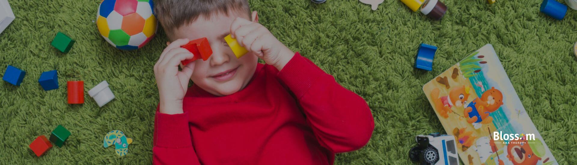 A young boy with autism playing on the floor with colorful toys and building blocks during ABA therapy activity.