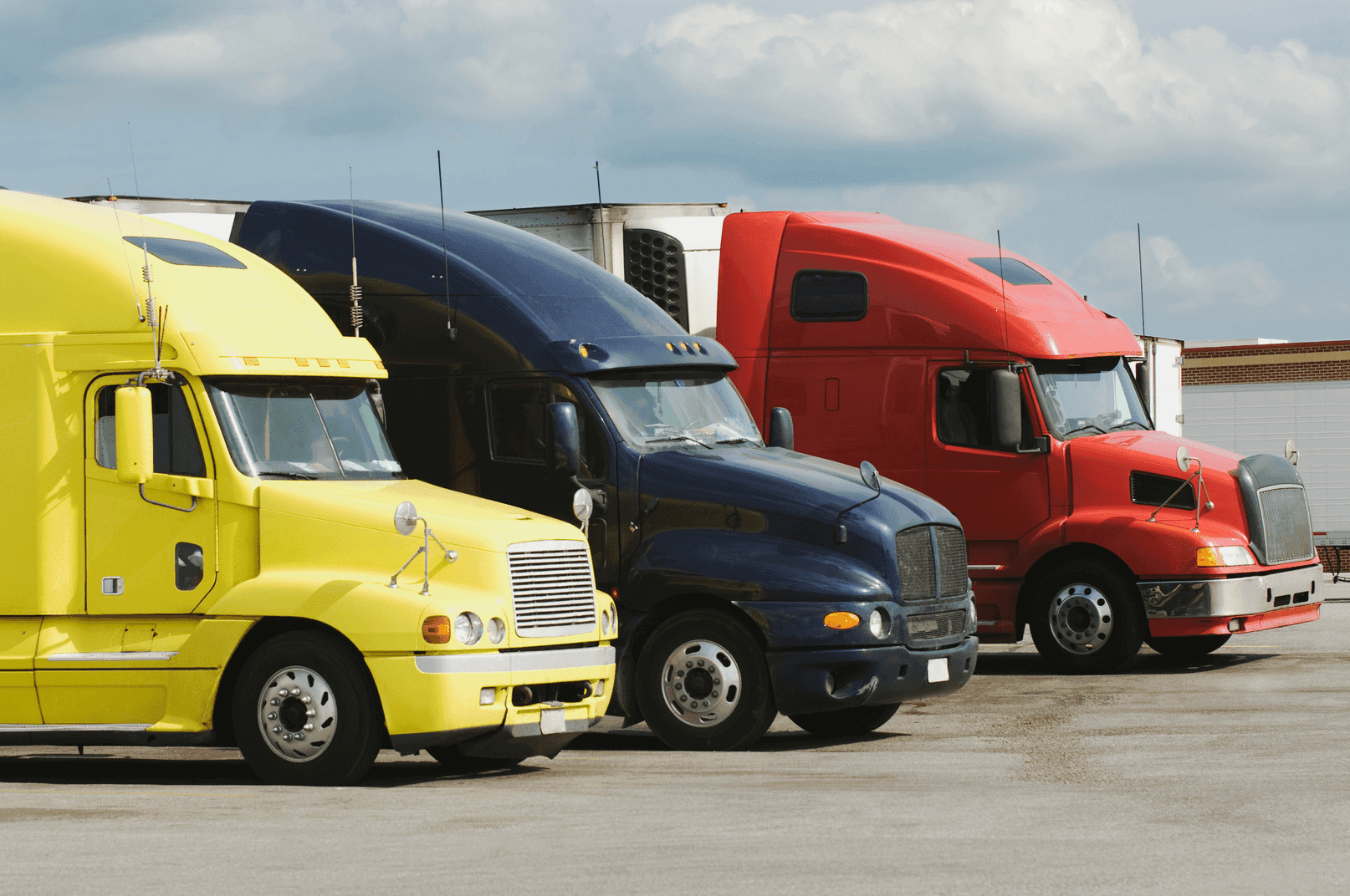 A photo of 3 identical trucks (yellow, blue and red) in profile, parked side by side in a shunting yard