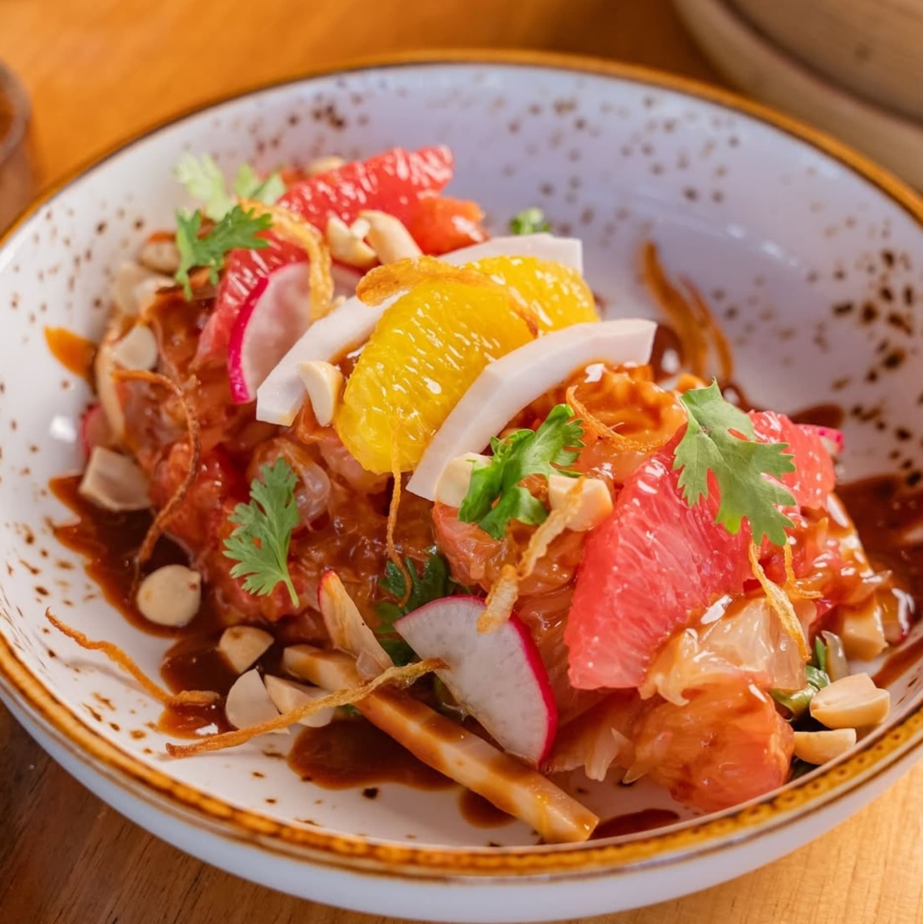 A vegan dish called Hello Pomelo Salad with citrus fruits, tender coconut, pink radish, peanuts, and miso soya dip served fresh.