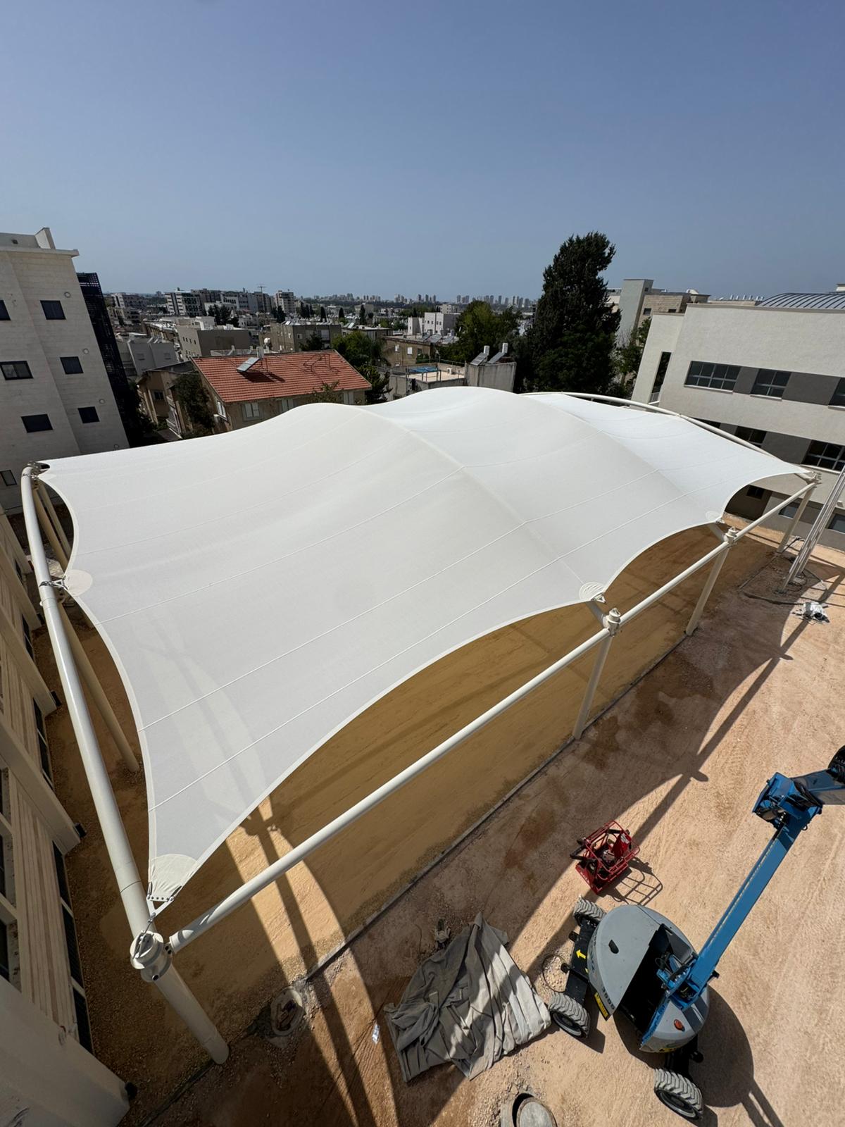 Large beige sunshade over a courtyard between multi-story buildings with construction equipment.