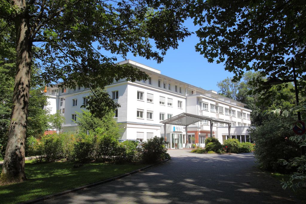 Clinique avec une façade blanche, entourée d'arbres matures et de végétation verte