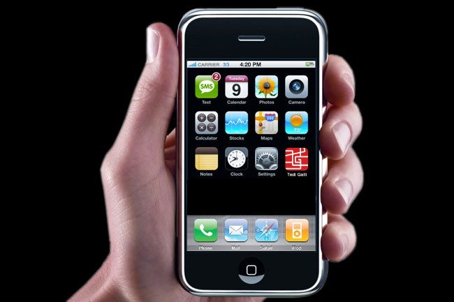 A hand holds a black iPhone displaying its home screen against a black background. The screen shows various app icons including Text, Calendar, Photos, Camera, Calculator, Stocks, Maps, Weather, Notes, Clock, Settings, and Teddy Gait. The time displayed is 4:20 PM, and the carrier is 33. The phone's bottom bar includes Phone, Mail, Safari, and iPod icons.