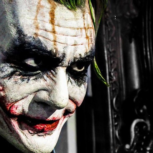 Nahaufnahme einer Person mit weißer Gesichtsbemalung, verschmiertem schwarzem Augen-Make-up und roten Lippen, die an die Joker-Figur erinnert.