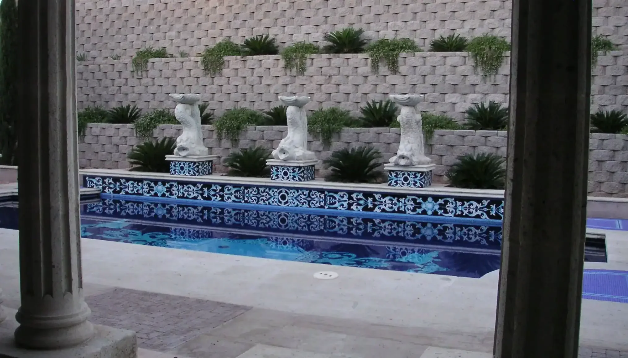 Custom mosaic tile pool design with intricate blue patterns and sculptures.