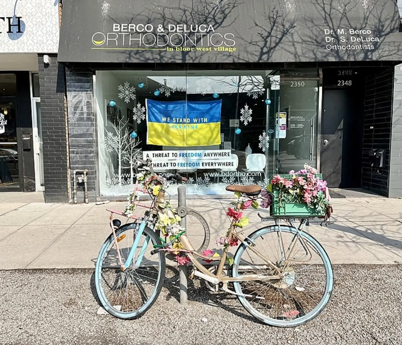 A blue bicycle covered in flowers in front of a shop in Bloor West Village.