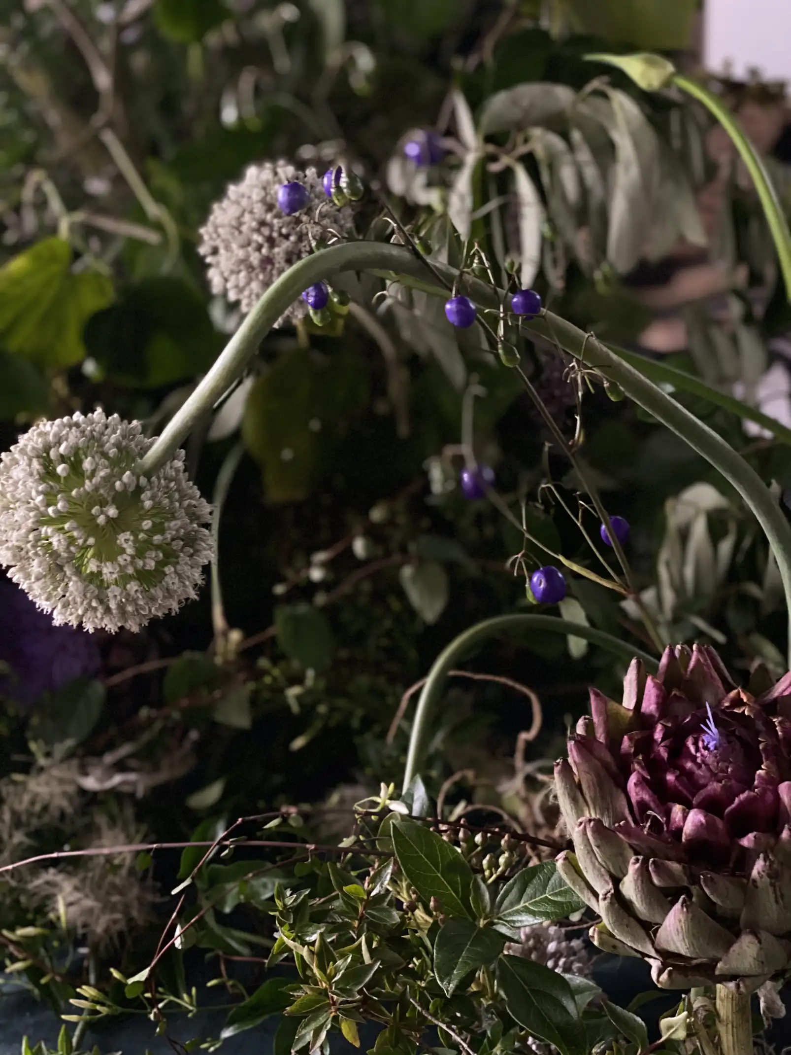 Arreglo floral con alcachofas y flores esféricas blancas y violetas para ambientación orgánica con contraste de texturas.