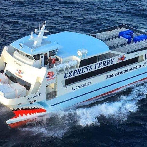 A white ferry named "Alexandre R" from "lineasromero.com" traveling through blue ocean water, with seating visible on the deck.