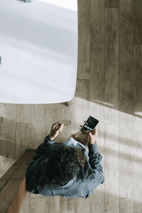 top down view of a man looking at their phone while holding their credit card