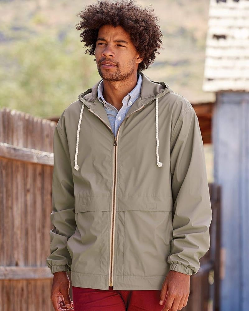 A beige zip up hooded rain jacket on a model that is walking past a fence.