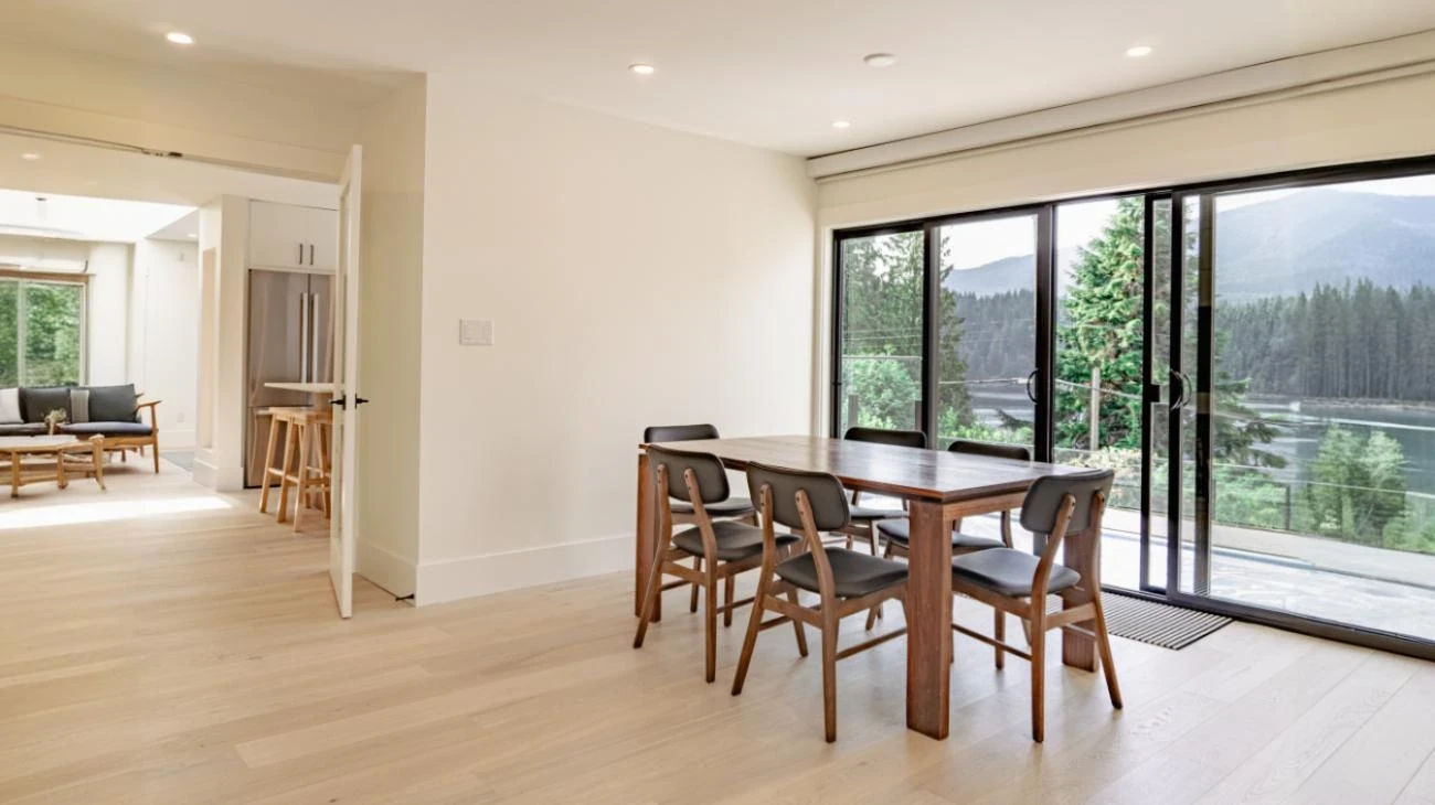 Modern dining area with solid wood table, designer chairs, and sliding glass doors leading to outdoor deck in Vancouver custom home