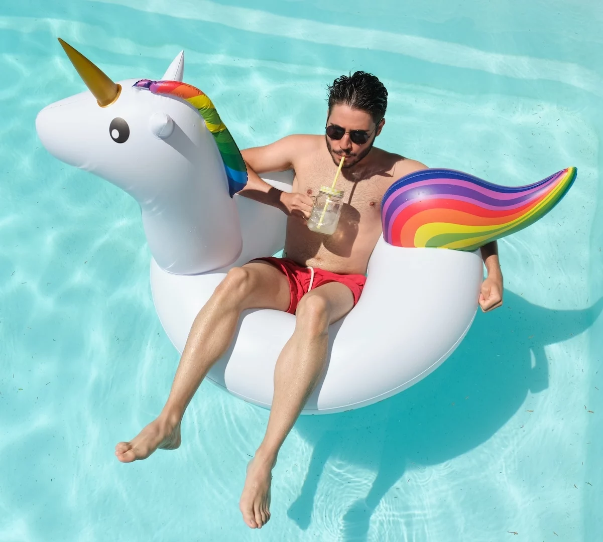 Man sitting in an inflatable unicorn in a pool, sipping on a drink