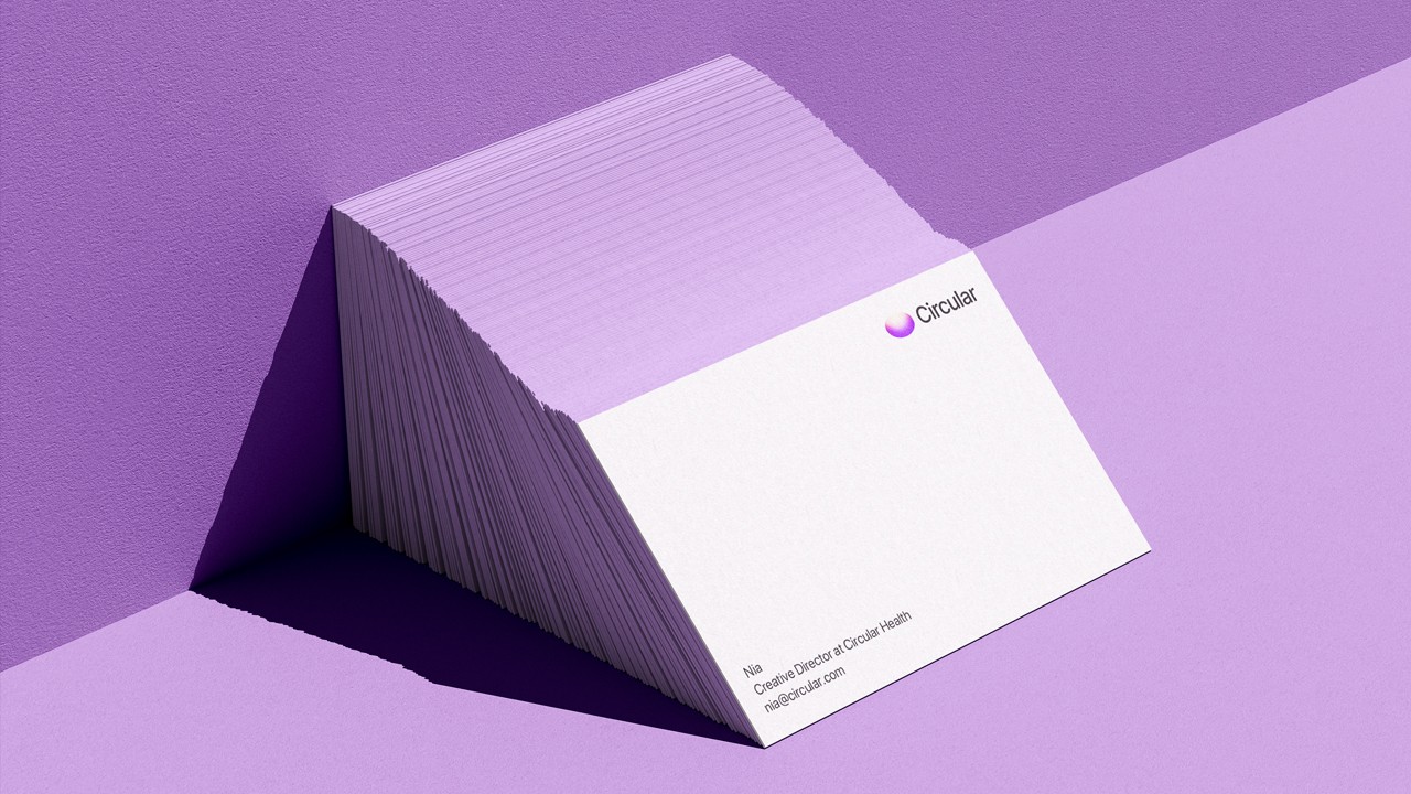 Angled stack of white business cards with lavender-coloured edges leaning against a purple wall; the top card shows a small gradient pill logo and “Circular” in the top right, plus contact details at the bottom.