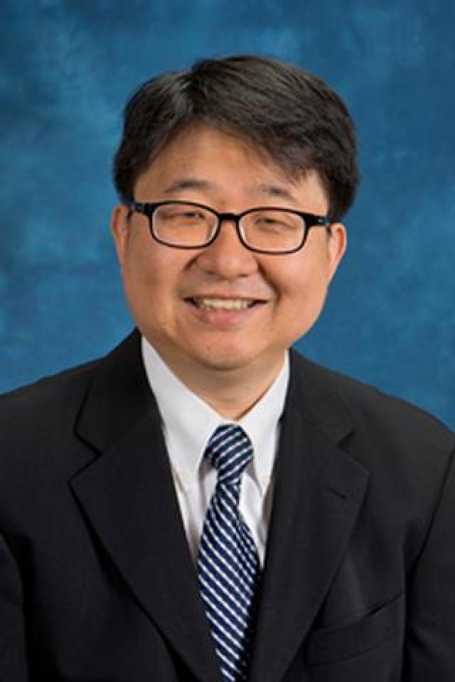Asian man in glasses and a suit smiling at the camera, wearing a tie. Official portrait