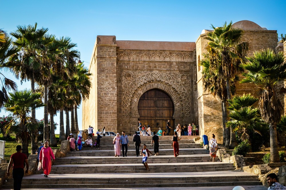 Visitors climbing stone steps to a historic Kasbah gate lined with palm trees in Morocco