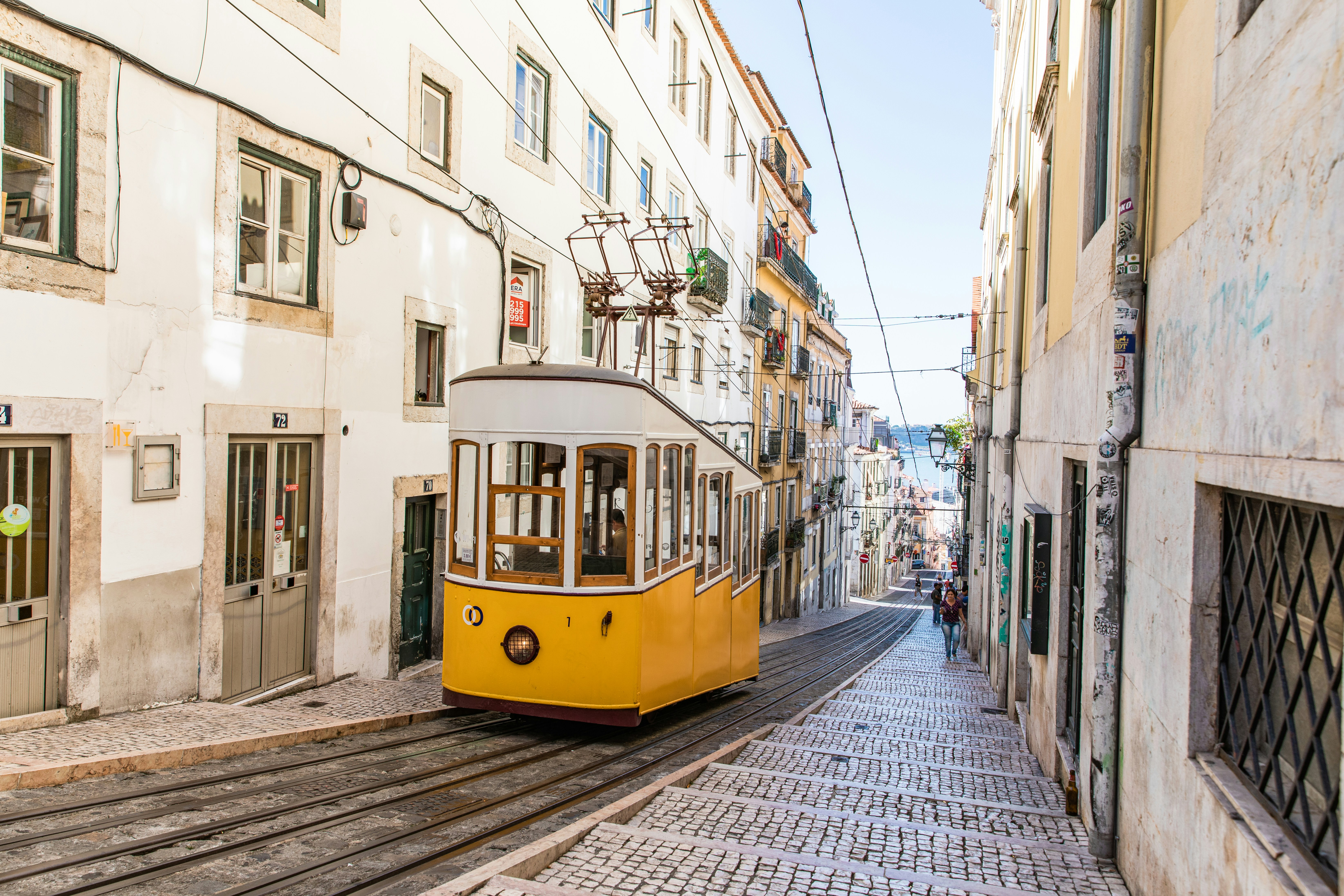 Tram in Lisbon going up a hill with the ocean in the background