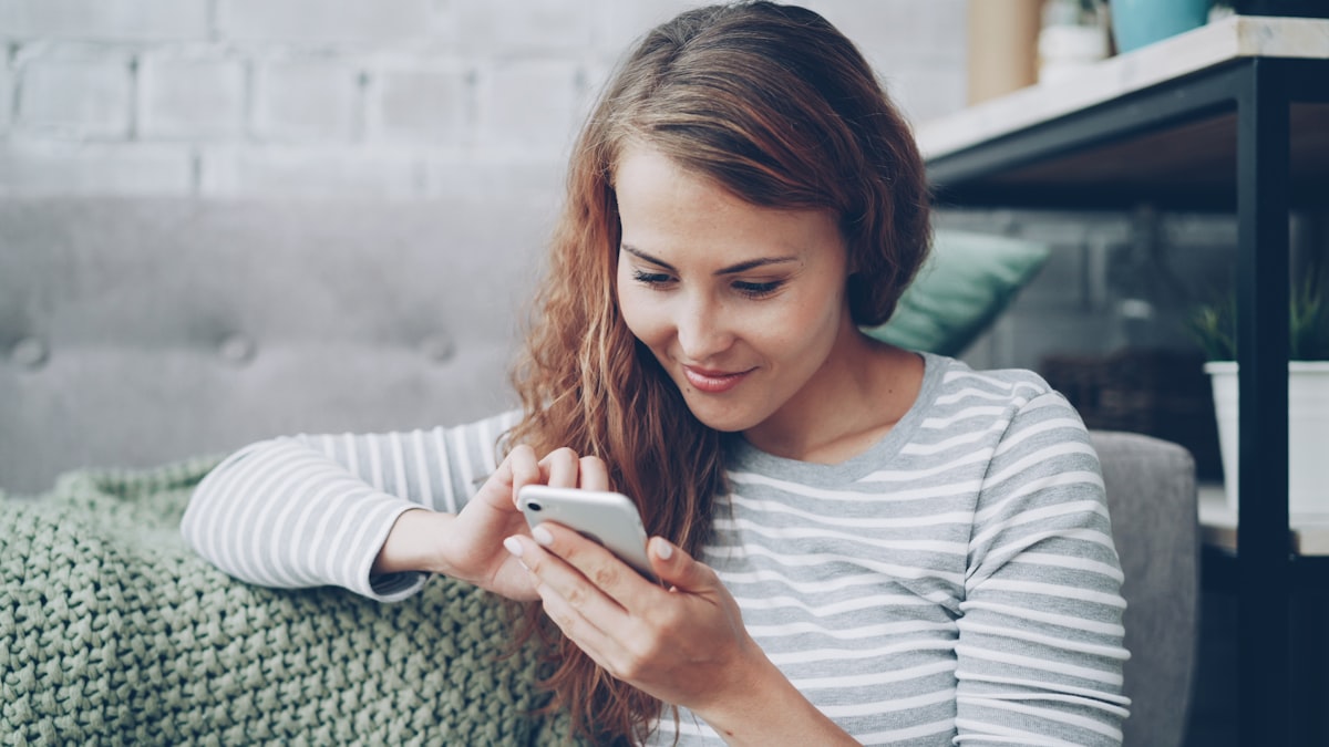 Woman smiling at her phone while planning a trip with an AI travel agent
